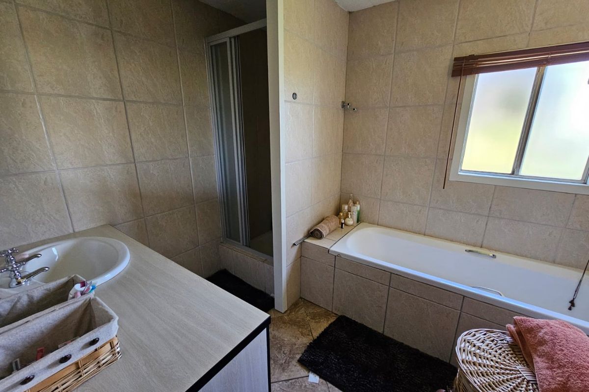 A functional bathroom featuring a built-in bathtub, separate shower enclosure, and a vanity basin with tiled walls and flooring.