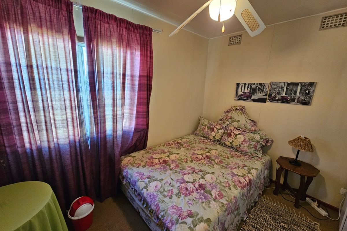 A compact bedroom featuring a ceiling fan, carpeted flooring, and a window with curtains.