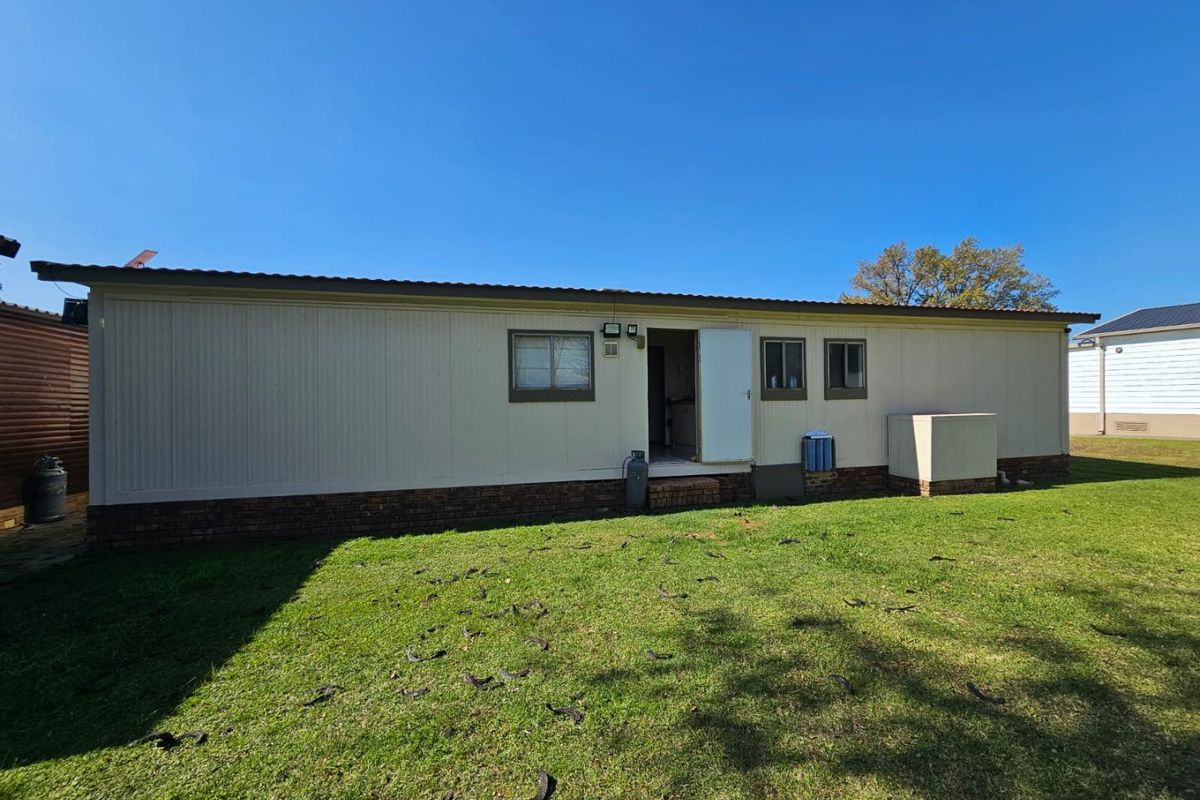 A view of the rear exterior elevation of the house, featuring metal cladding, brick base, and a lawn area.