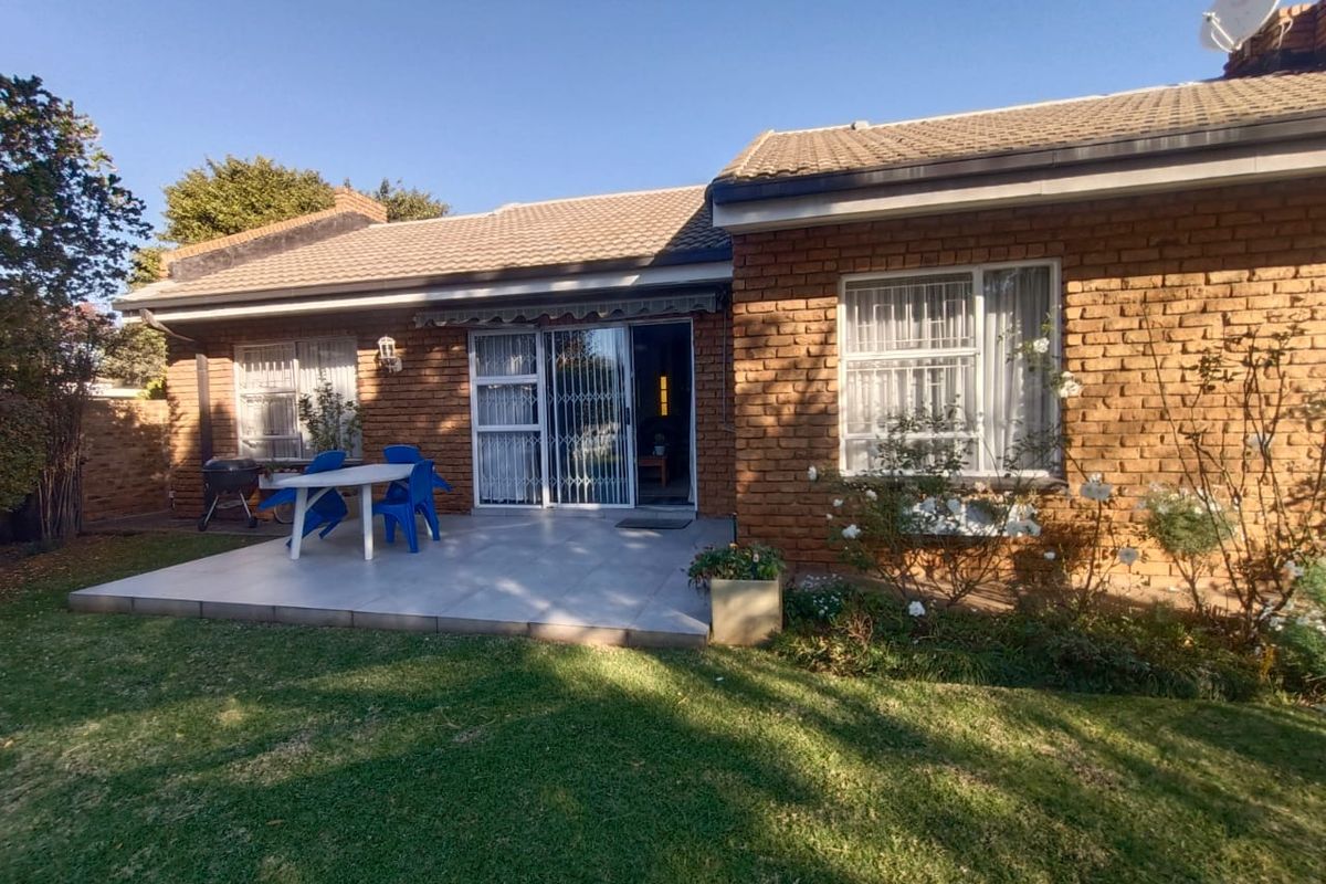 Rear view of the townhouse featuring a paved patio area, brick facade, tiled roof, and a well-maintained garden.