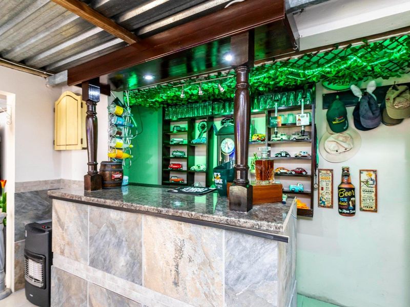 A dedicated home bar area featuring a stone-clad counter with a granite top, built-in display shelving, and industrial-style exposed ceiling finishes.