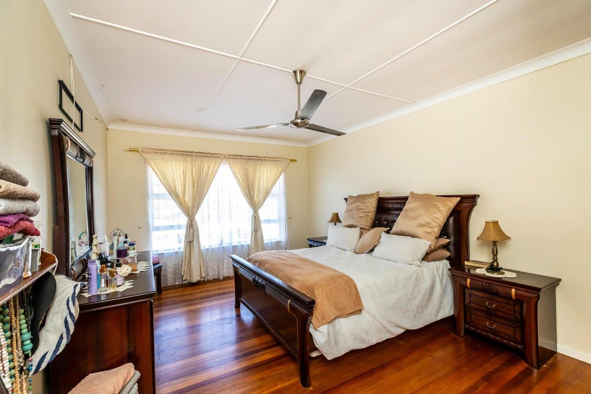 A spacious bedroom featuring polished hardwood flooring, a ceiling fan, and a coved ceiling, offering a comfortable and classic living space.