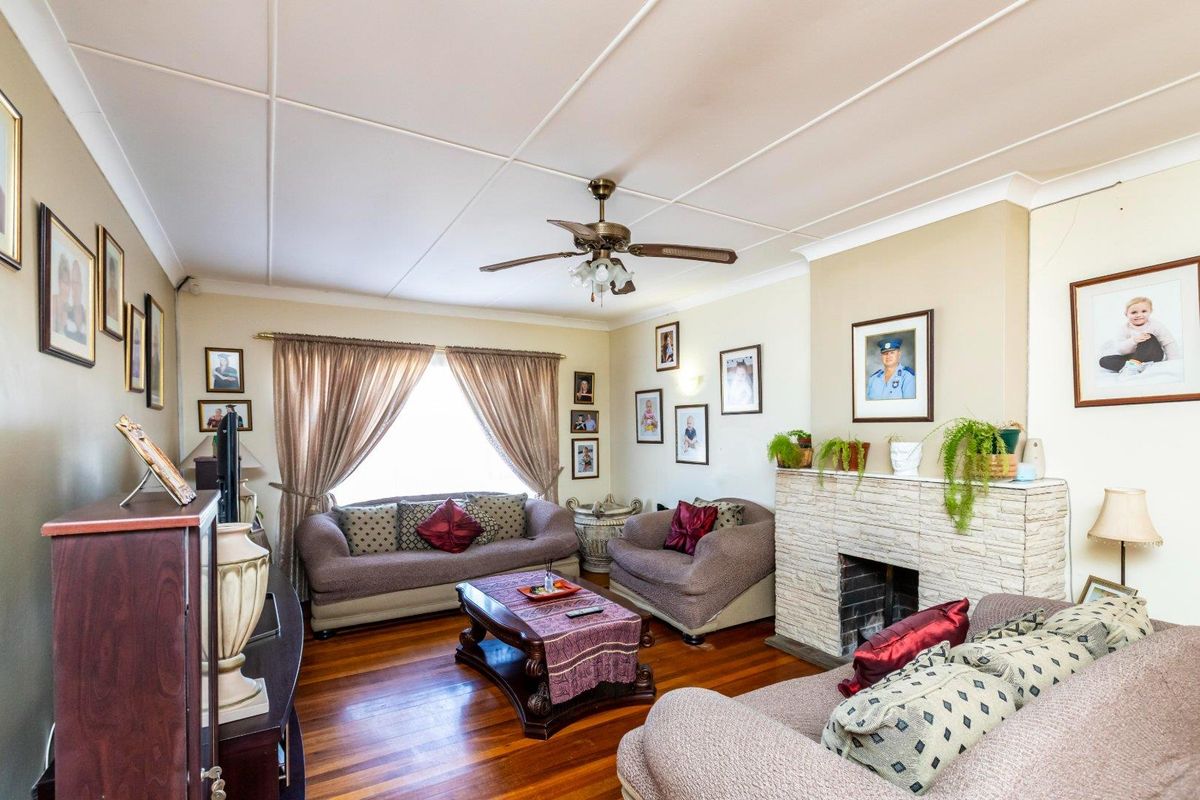 A cozy living room featuring hardwood flooring, a stone fireplace, and a ceiling fan, offering a warm and traditional atmosphere.