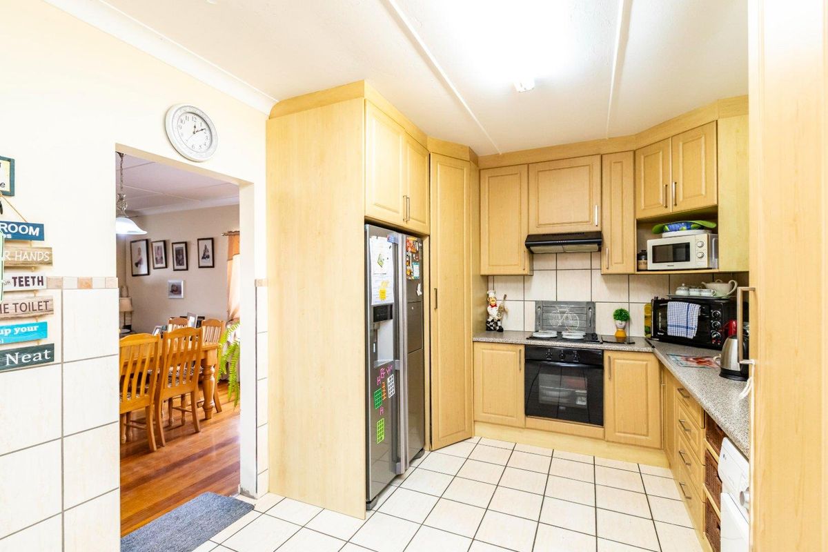 Functional kitchen featuring light wood cabinetry, tiled flooring, built-in oven, hob, and extractor fan, with an open-plan flow into the adjacent dining area.