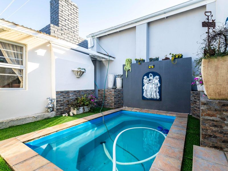 A compact outdoor pool area featuring a small swimming pool with tiled coping, artificial grass surround, and a decorative stone-clad feature wall.