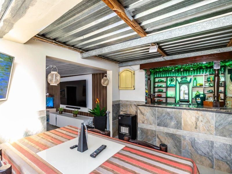 A rustic indoor bar area featuring stone-clad counter, built-in shelving, and an exposed corrugated metal ceiling with timber beams.