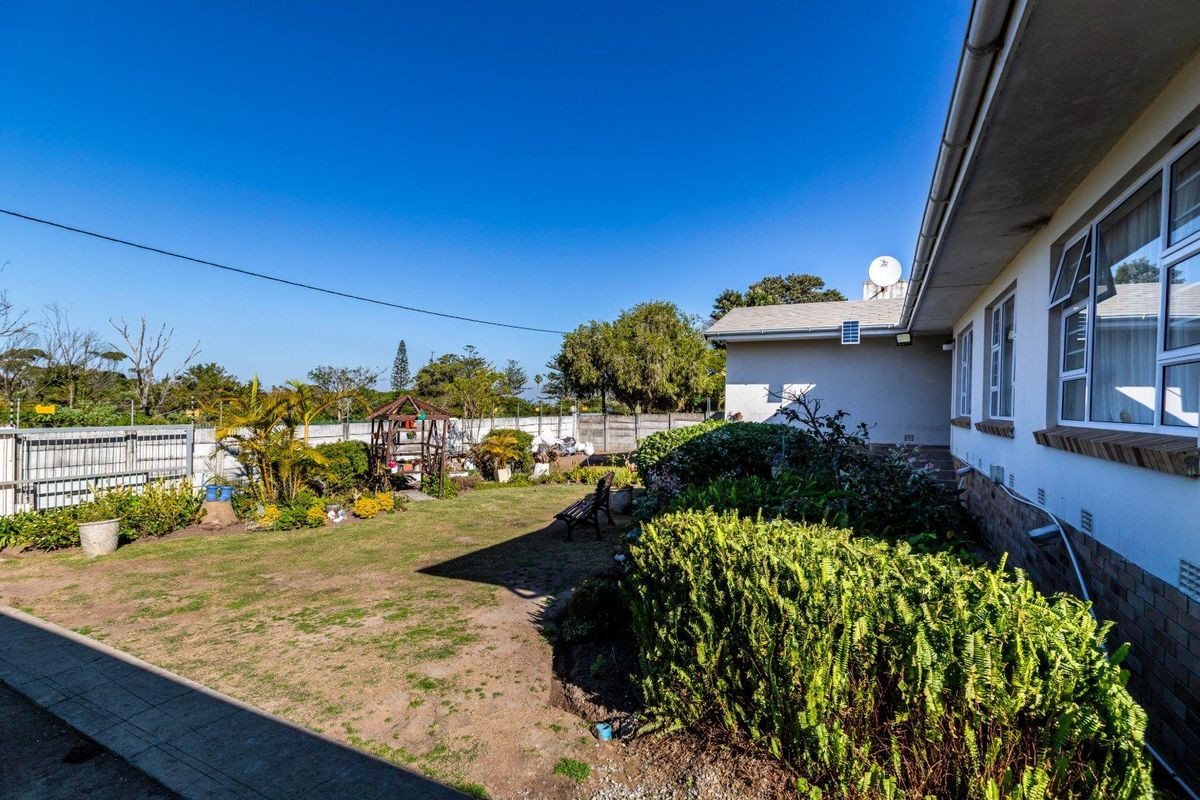 A view of the rear garden featuring a lawn area, established garden beds, and the side elevation of the house with aluminium windows.