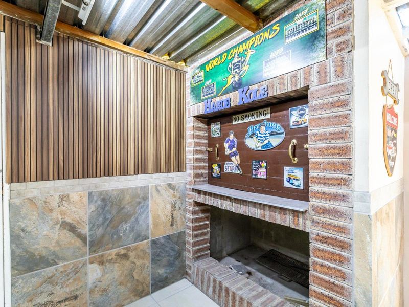 Covered outdoor patio area featuring a built-in brick braai, slate tile accents, and timber wall paneling under a corrugated metal roof.