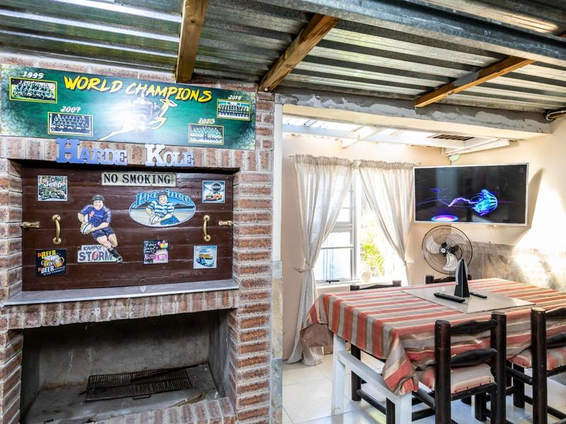 Covered outdoor patio area featuring a built-in brick braai, corrugated iron roofing, and exposed timber rafters, suitable for casual outdoor dining and entertainment.