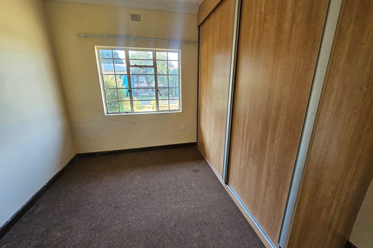 A bedroom featuring built-in wooden sliding door cupboards, carpeted flooring, and a window providing natural light.