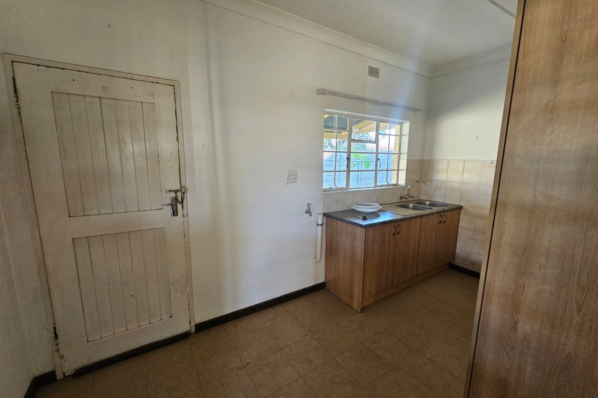 A functional kitchen area featuring basic cabinetry, a double sink, tiled splashback, and tiled flooring, offering potential for modernization.