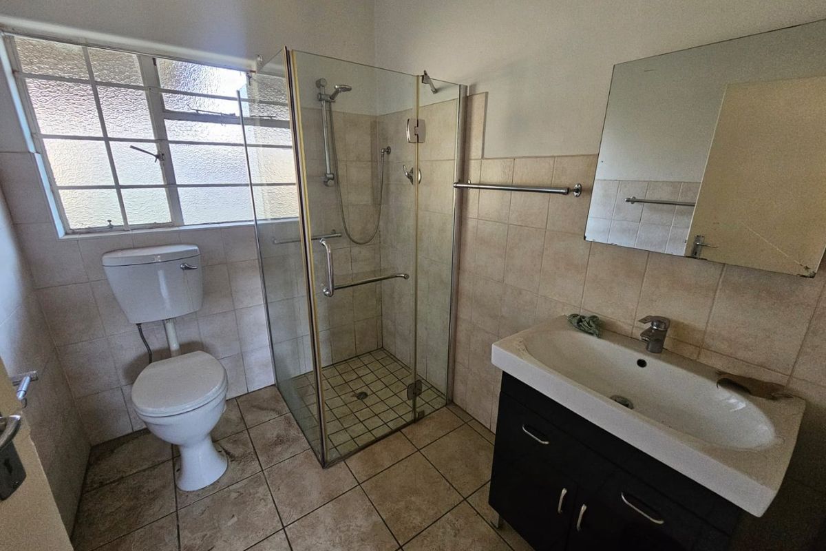 A functional bathroom featuring a glass-enclosed shower, a vanity basin with storage, and a standard toilet, finished with neutral wall and floor tiles.