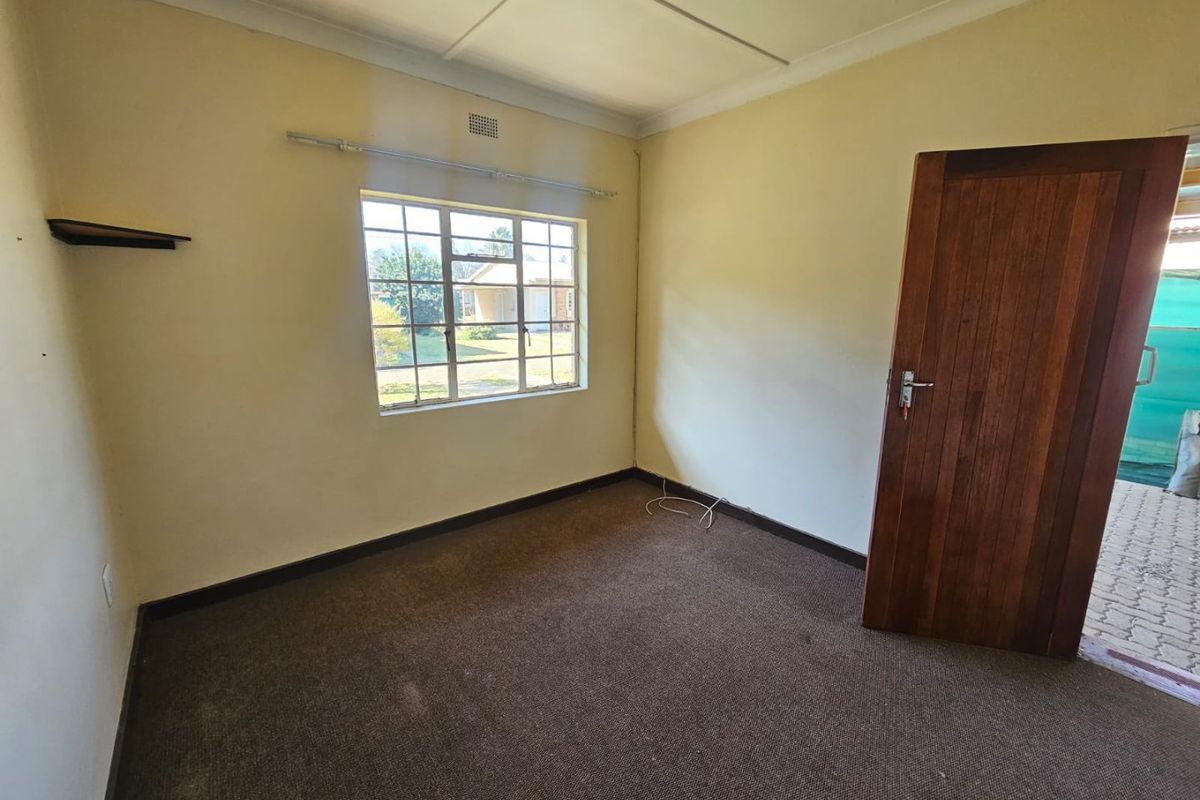 A vacant bedroom featuring brown carpeting, a wooden door, and a window overlooking the exterior.