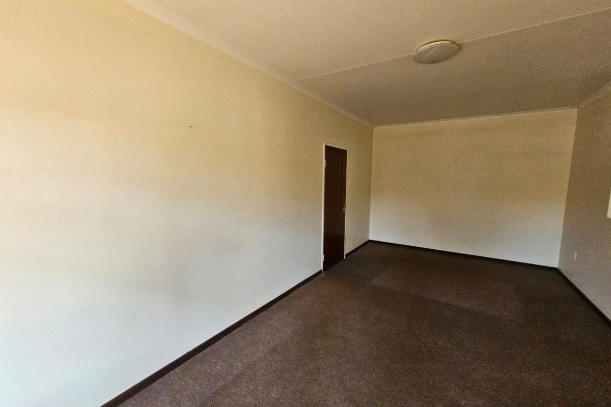 An empty, neutrally painted living room featuring brown carpeting and a standard interior door, offering a blank canvas for potential renovation.