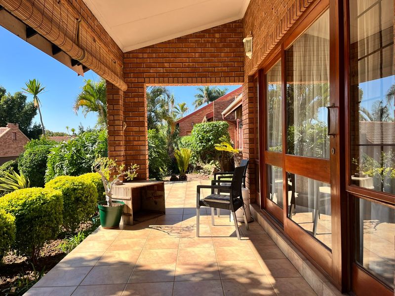 A covered patio area featuring exposed brick pillars, tiled flooring, and large timber-framed sliding doors providing access to the garden.