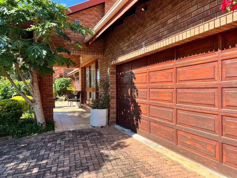 Front exterior view of a brick house featuring a paved driveway, a covered entrance patio, and a wooden garage door.