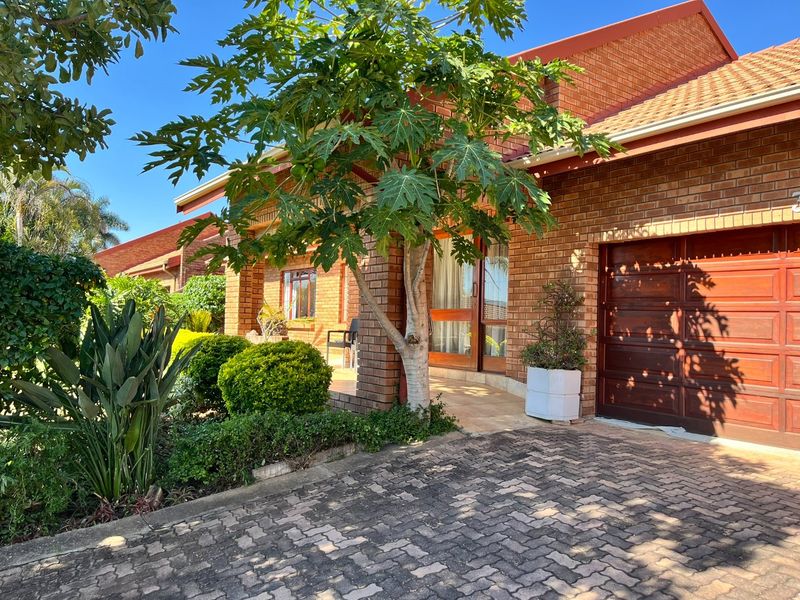 Front elevation of a face brick house featuring a paved driveway, covered entrance, and a wooden garage door.