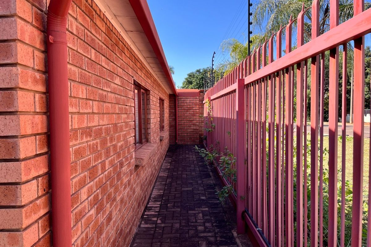 A side walkway featuring face brick exterior walls, paved flooring, and secure metal perimeter fencing with integrated electric security wires.