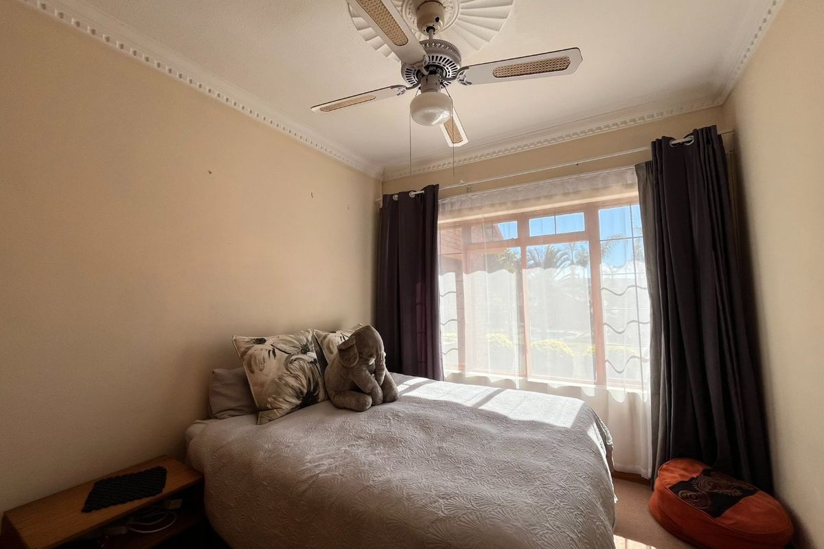 A bedroom featuring a ceiling fan with a decorative rose, ornate cornice detailing, and a large window allowing for natural light.