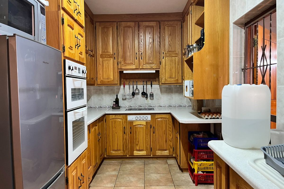 A functional kitchen featuring traditional wooden cabinetry, built-in oven and hob, tiled backsplash, and durable tiled flooring.