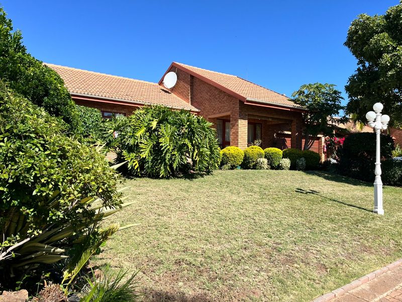 A well-maintained brick house exterior featuring a tiled roof, established garden, and a front lawn area.