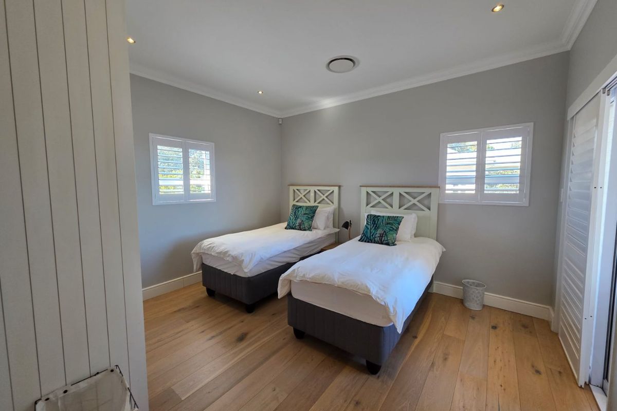 A well-maintained bedroom featuring light timber flooring, plantation shutters, recessed downlighting, and neutral wall finishes.