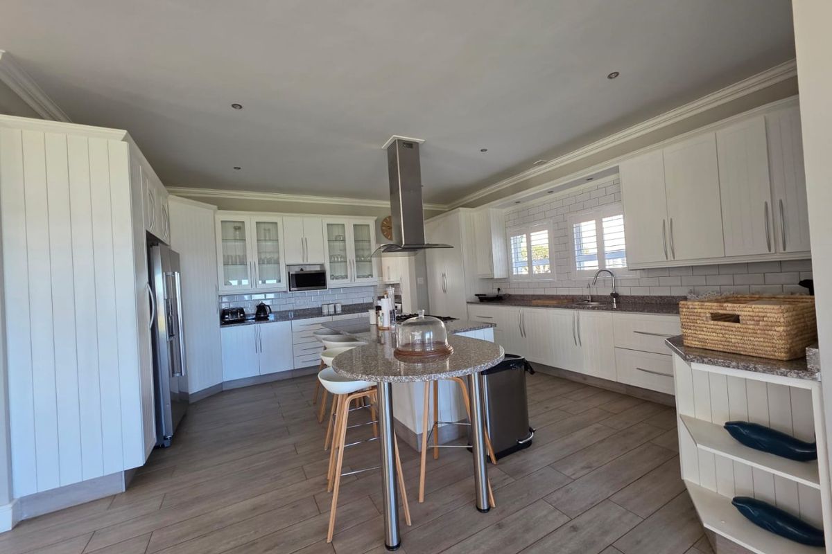 Spacious modern kitchen featuring white cabinetry, granite countertops, a central island with breakfast bar, stainless steel extractor fan, and wood-look tiled flooring.
