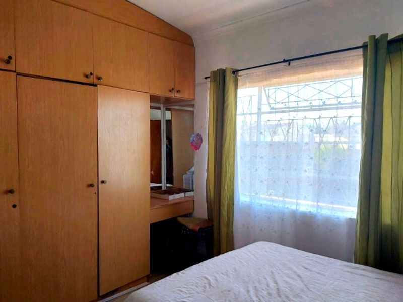 Bedroom featuring extensive built-in wooden cabinetry with an integrated vanity unit and a window fitted with security bars.