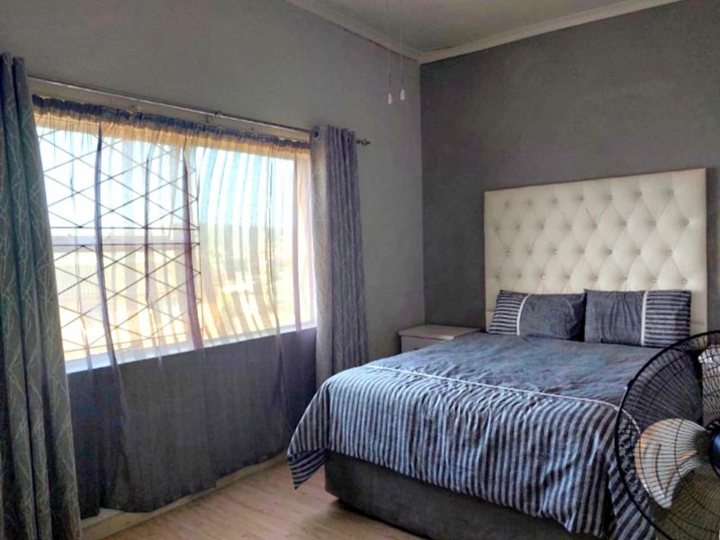 A bedroom featuring laminate flooring, a ceiling fan, and a large window with curtain rails, providing a functional and comfortable sleeping space.