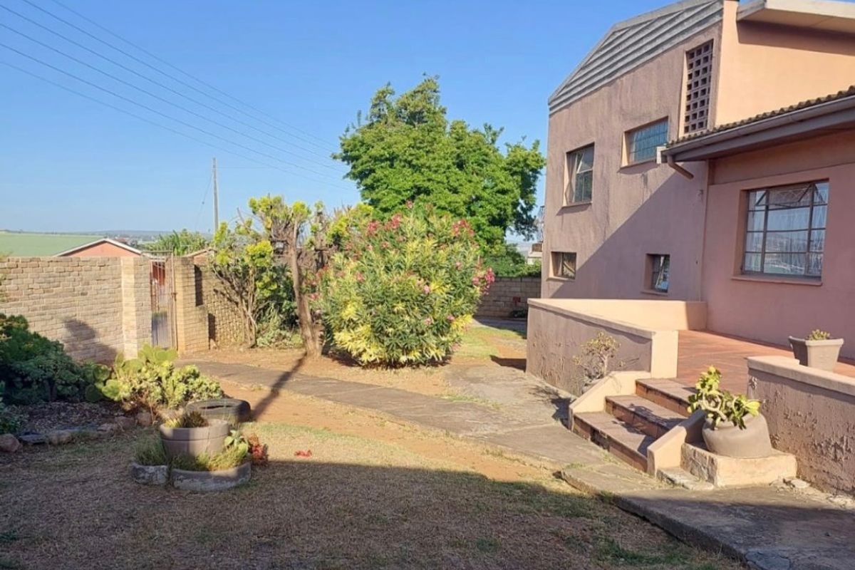 Rear view of the property featuring a paved patio area, concrete steps, and a garden with a brick boundary wall.