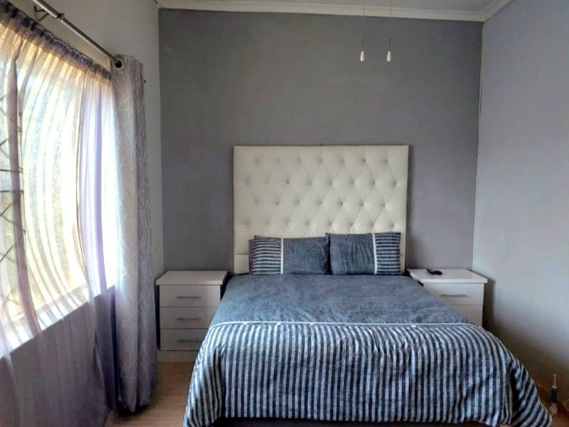 A bedroom featuring laminate flooring, a grey accent wall, and neutral finishes, providing a comfortable and functional sleeping space.