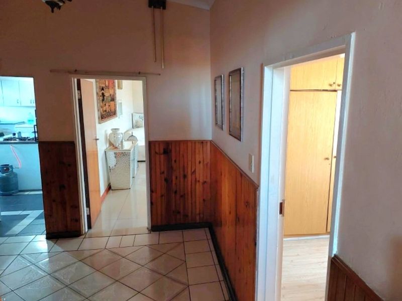 A hallway featuring timber wall paneling and ceramic floor tiles, providing access to adjacent rooms including a kitchen and bedroom area.