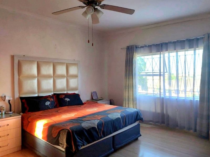 A bedroom featuring laminate flooring, a ceiling fan, and a window fitted with security bars.