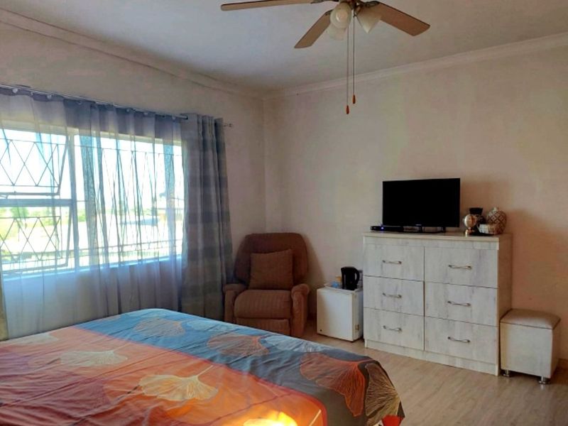 A bedroom featuring laminate flooring, a ceiling fan, and a window fitted with security bars.