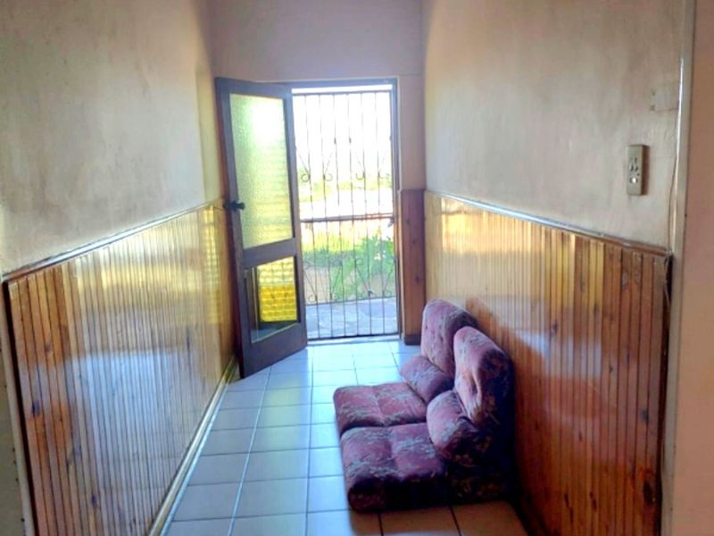 A narrow hallway featuring timber wall paneling, a timber ceiling, and tiled flooring, leading to an exterior door with a security gate.