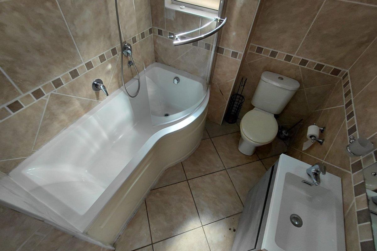 Compact bathroom featuring a curved shower-bath combination, wall-mounted toilet, and a modern vanity basin with neutral wall and floor tiling.