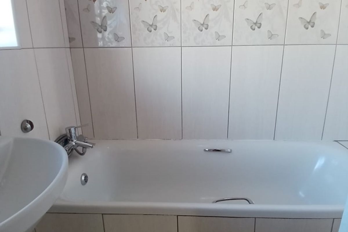 A functional bathroom featuring a standard bathtub with a tiled side panel and decorative butterfly-patterned wall tiles.