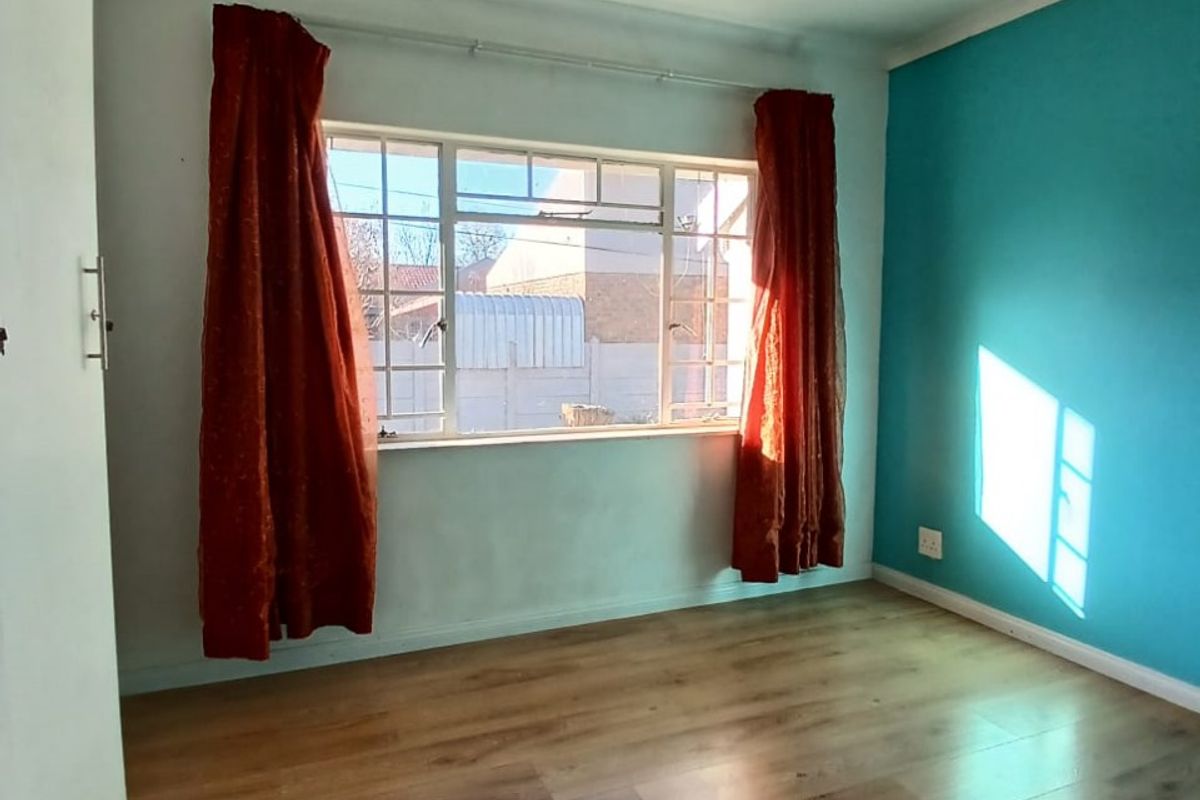 A bright bedroom featuring wood-look laminate flooring, a large window with natural light, and a bold blue accent wall.