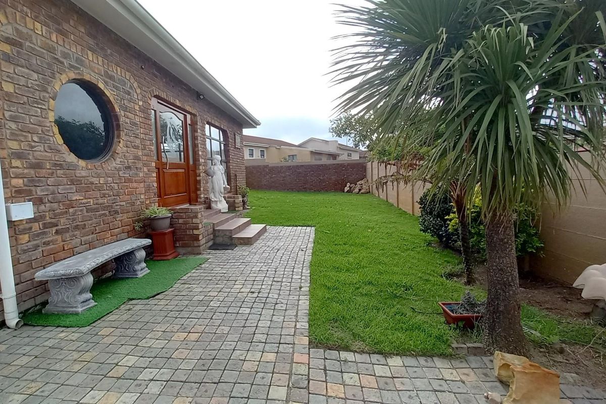 A rear garden area featuring a brick facade, paved walkway, lawn, and perimeter boundary walls.