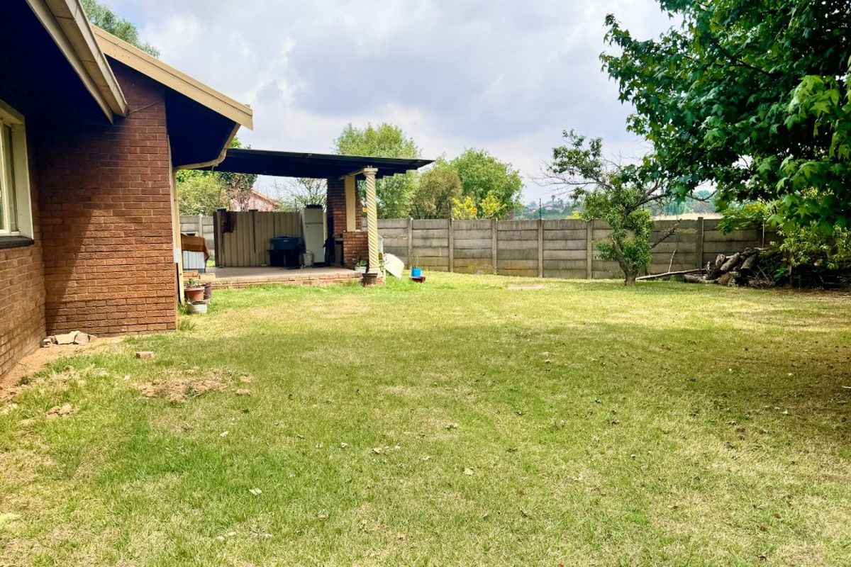 Spacious rear garden featuring a lawn area and a covered patio space, enclosed by perimeter walling.