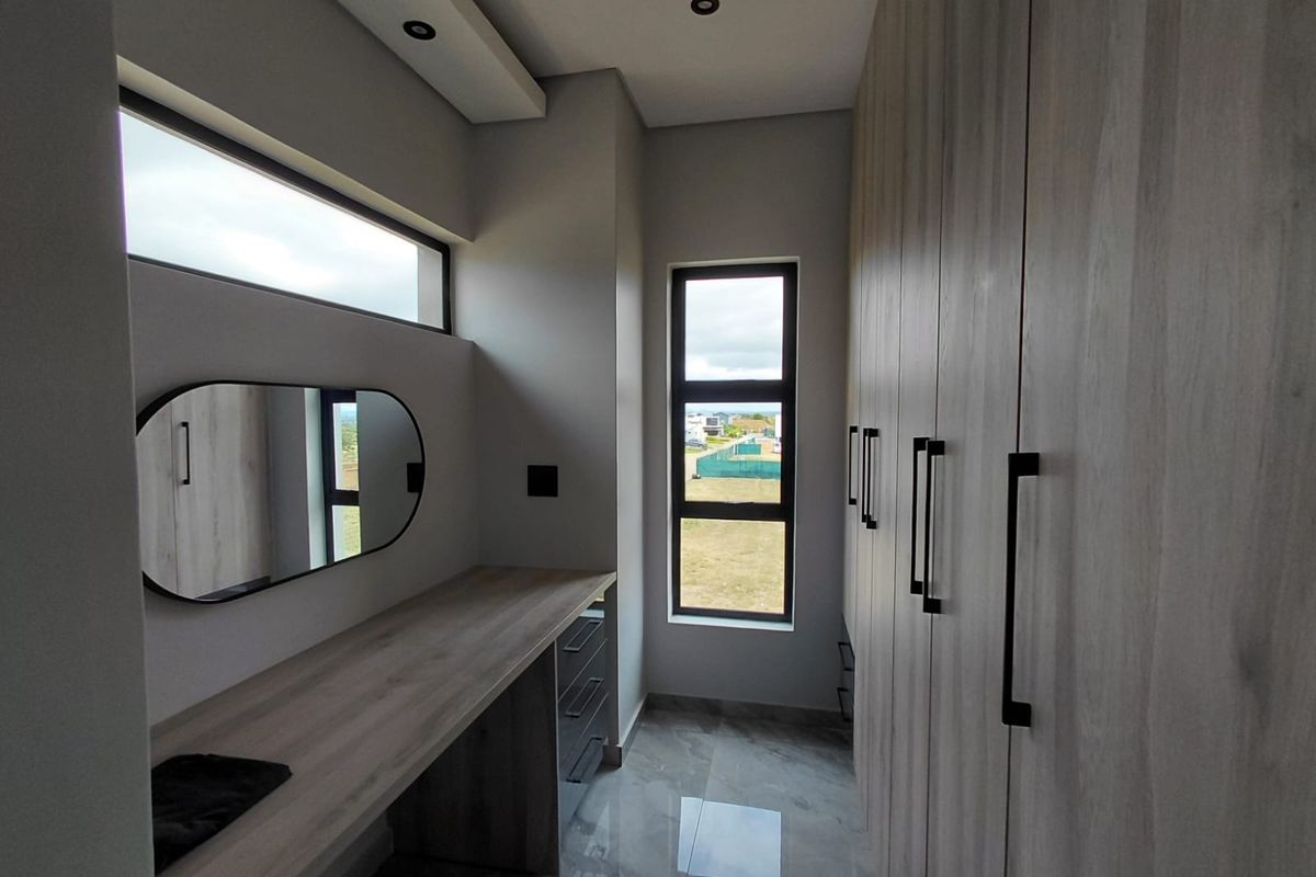 A modern dressing room featuring extensive built-in cabinetry, a sleek vanity desk, recessed ceiling lighting, and large windows with natural light.