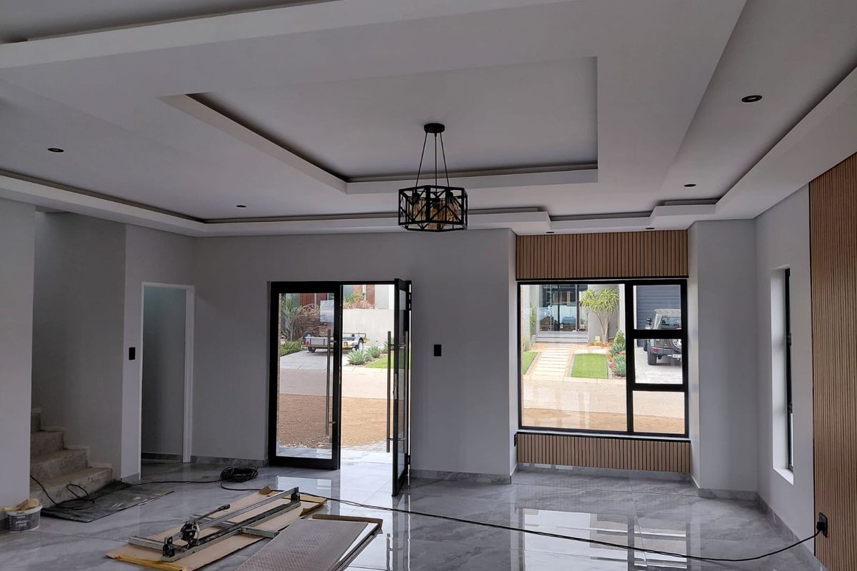 Spacious living area featuring modern recessed tray ceiling, large windows, sleek tiled flooring, and contemporary timber slat wall paneling.