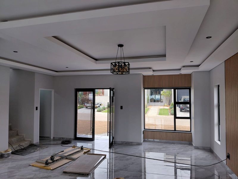 Spacious living area featuring modern recessed tray ceiling, large windows, sleek tiled flooring, and contemporary timber slat wall paneling.