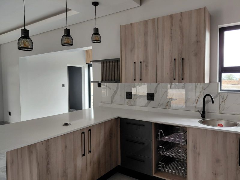 Modern kitchen featuring light wood-grain cabinetry, contrasting dark grey drawers, marble-look splashback, stone countertops, and contemporary pendant lighting.