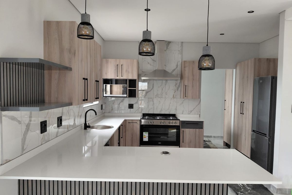 Modern kitchen featuring light wood cabinetry, white stone countertops, marble-look backsplash, built-in oven, extractor fan, and contemporary pendant lighting.