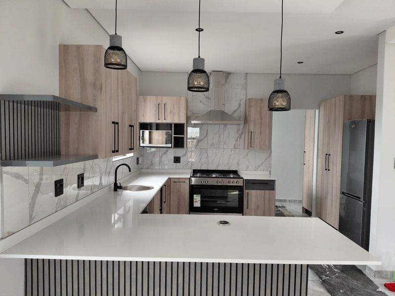 Modern kitchen featuring light wood cabinetry, white stone countertops, marble-look backsplash, built-in oven, extractor fan, and contemporary pendant lighting.