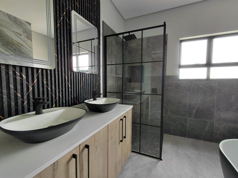 Modern bathroom featuring a double vanity with vessel sinks, black fixtures, and a walk-in shower with a black-framed glass screen.