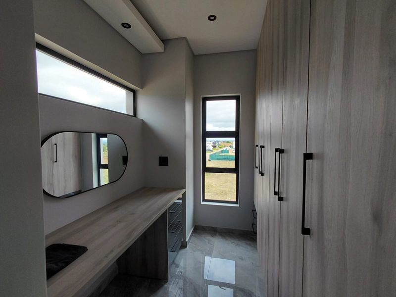 A modern dressing room featuring extensive built-in cabinetry, a sleek vanity desk, recessed ceiling lighting, and large windows with natural light.