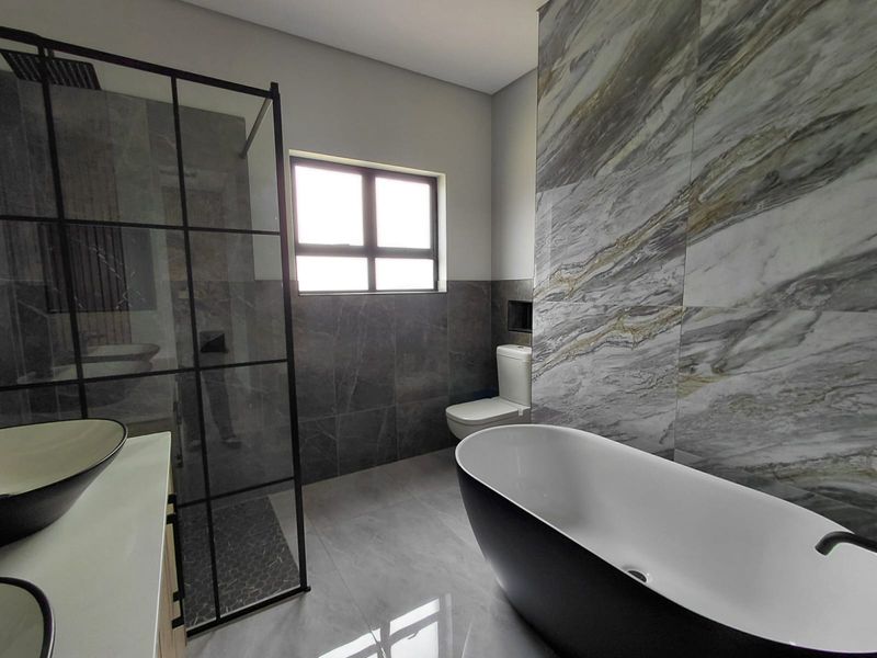 Modern bathroom featuring a freestanding bathtub, a walk-in shower with a black frame, and elegant marble-style wall tiling.