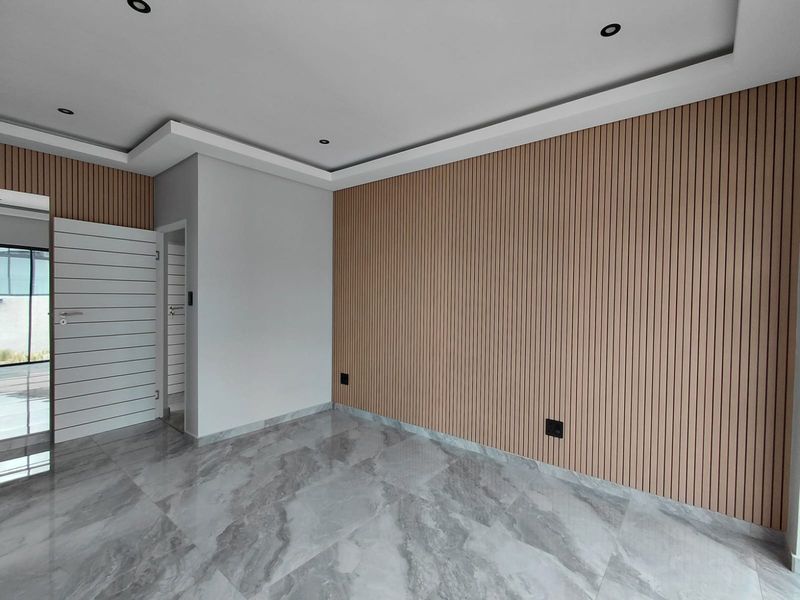 A modern, empty room featuring contemporary wood-slat wall paneling, polished marble-look floor tiles, and recessed ceiling lighting with a tray ceiling design.